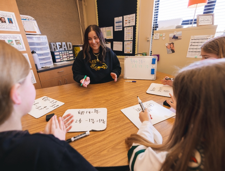 Teacher working with two students at a desk.