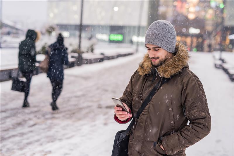 Man on snowy sidewalk using his phone.